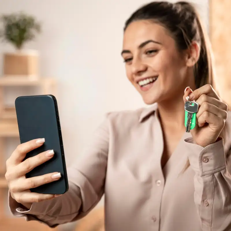 Mulher sorridente segurando as chaves de um imóvel e o celular