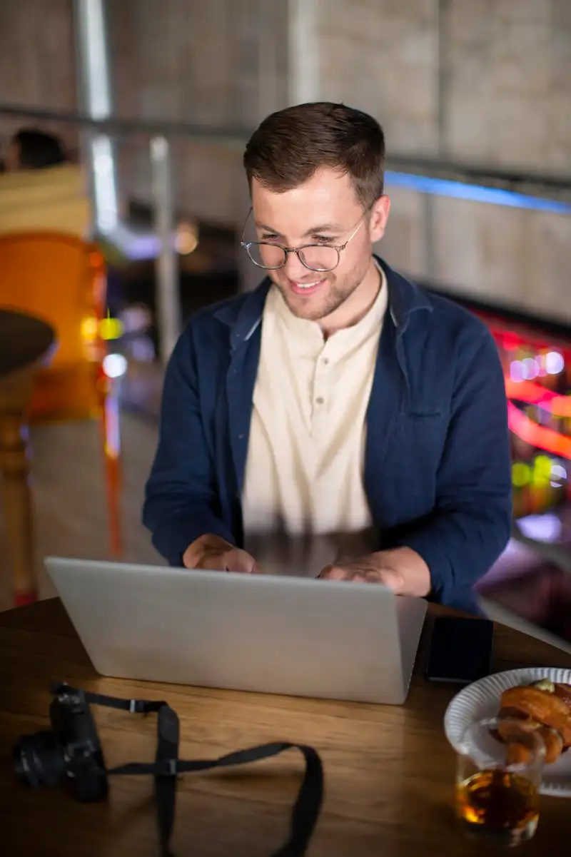 Homem de óculos sorrindo enquanto usa um notebook em uma mesa de café