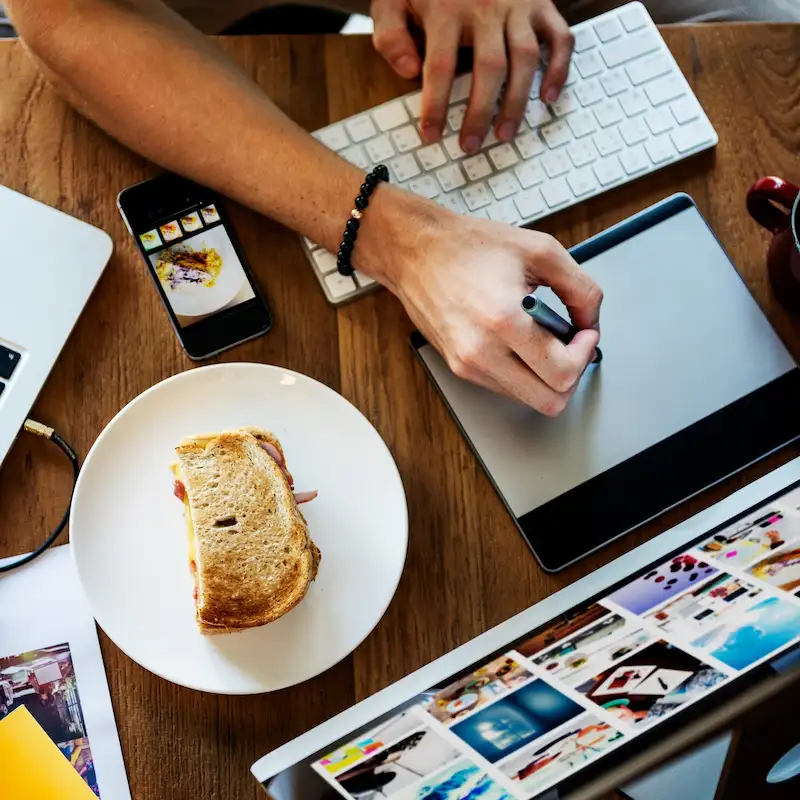 Vista de cima de uma mesa com teclado, mesa digitalizadora, celular e um notebook com uma galeria de imagens