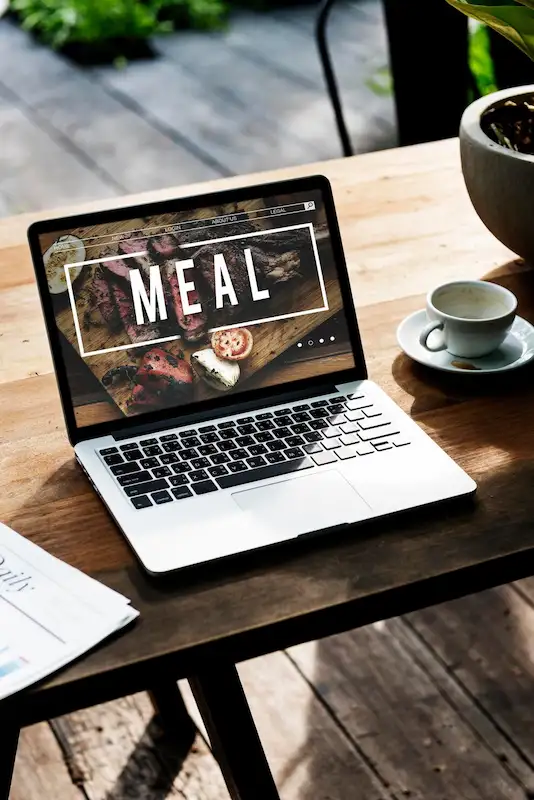 Notebook sobre uma mesa de madeira exibindo a página de um restaurante, ao lado de uma xícara de café