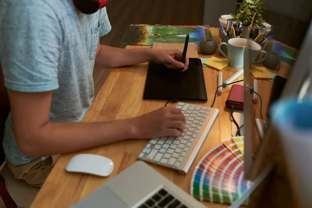 Designer usando mesa digitalizadora e teclado, com uma cartela de cores sobre a mesa de madeira