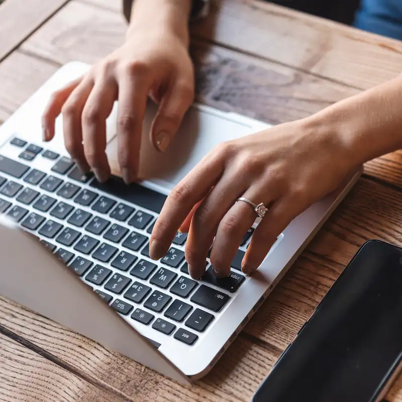 Mãos com um anel digitando em um notebook sobre uma mesa de madeira