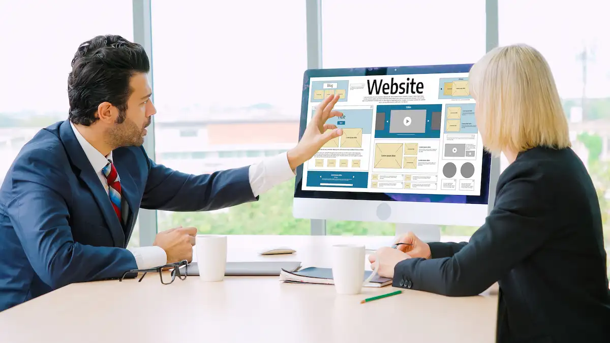 Homem de terno mostrando o layout de um site no monitor para uma colega, em um escritório