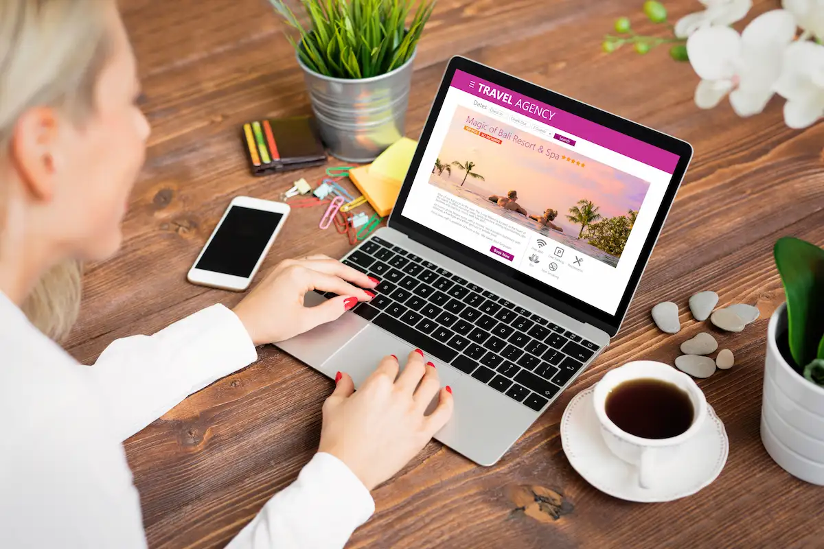 Pessoa digitando em um notebook com um site aberto na tela, ao lado de uma xícara de café